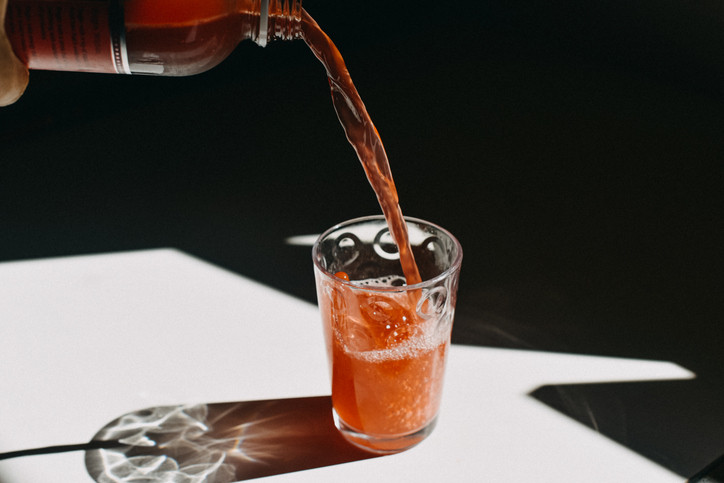 A red-colored drink being poured from a bottle into a glass with ice; concept is collagen drinks