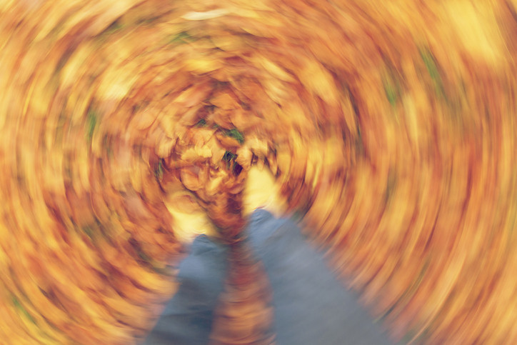 Swirling, blurred photo of person's legs standing in leaves; concept of dizziness