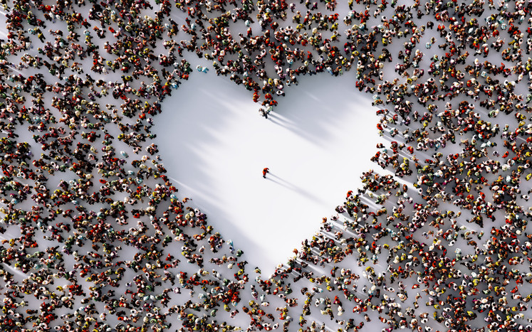 A high, overhead view looking down on a large crowd of tiny people and one tiny person standing alone in an empty, white, heart-shaped space 