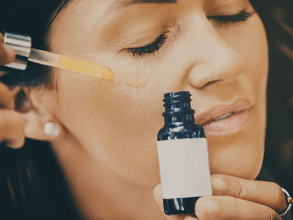 A woman applying Vitamin C serum to her face using a dropper