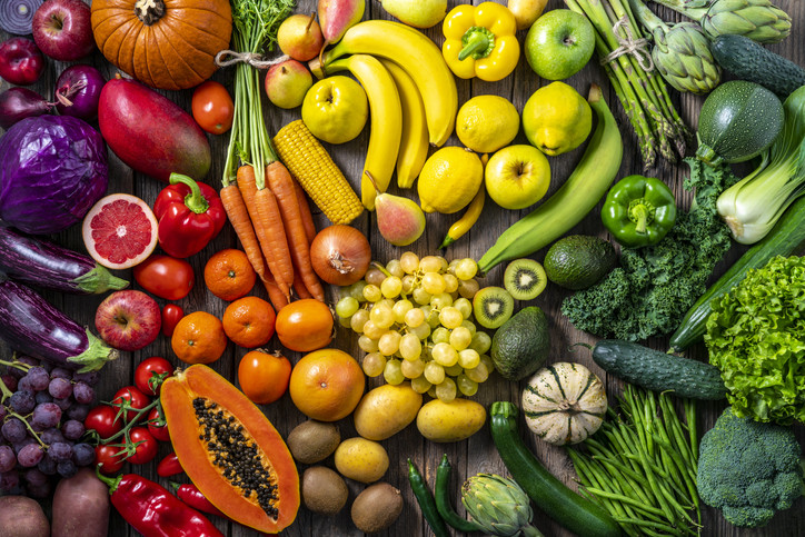 A collection of fruits and vegetables organized by color, including eggplants, pumpkins, grapefruit, oranges, tomatoes, papaya, bananas, lemons, asparagus, kale 