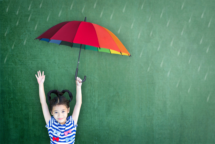 A smiling child with her arms up, holding a colorful umbrella 