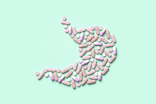 photo of an assortment of pills in different shapes and colors, arranged in the shape of a human stomach on a mint green background