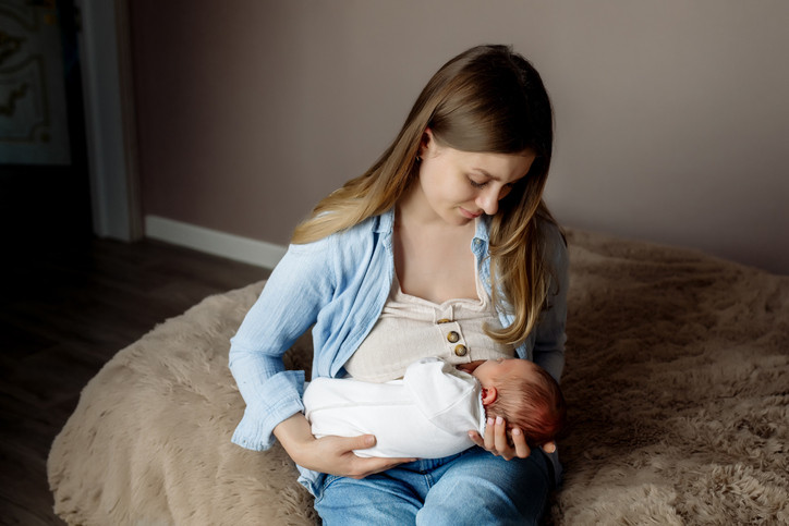 Woman seated on a bed breastfeeding her newborn baby