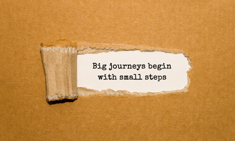 Cardboard with a piece peeled away, revealing text underneath that reads, big journeys begin with small steps