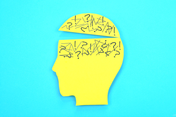 Concept of confusion, yellow cutout of head with scribbles and question marks in brain and top of head opening; turquoise blue background 