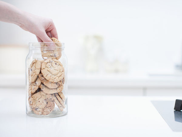 A hand reaching into a cookie jar that's on a kitchen counter