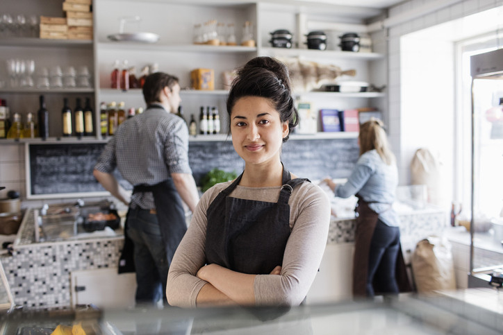 Owner of fish store dressed in apron with her arms crossed in foreground with a male and female employee in the background