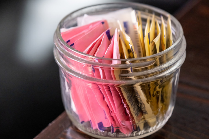 Small glass bowl full of assorted artificial sweetener envelopes.