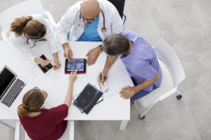 A group of physicians sitting at a table, all looking at information on a tablet