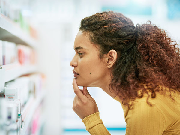 The sideview of a woman bending over to look closely at products on a store shelf, her hand is on her chin in contemplation