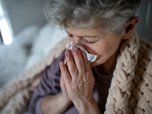 Photo of a sick senior woman in bed at home, sneezing and blowing her nose.