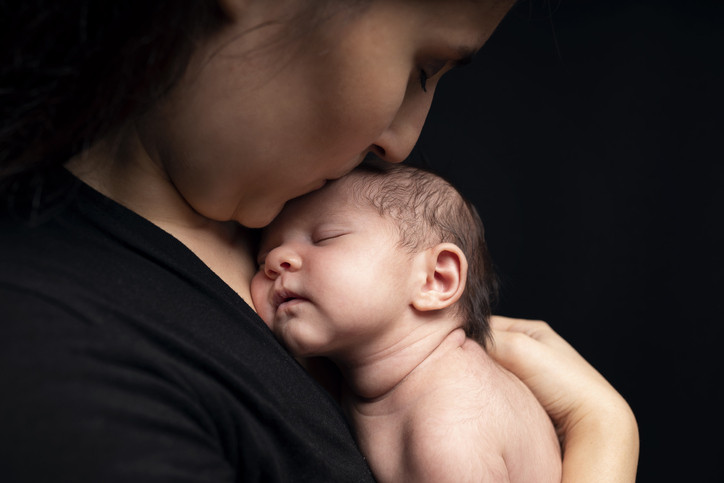 A mother holding and kissing the head of her newly born baby, black background