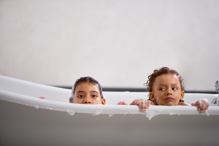 Two children in a bathtub, only their heads are visible over the side of the tub