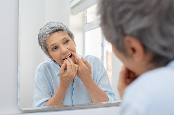 Mature beautiful woman cleaning her teeth with floss in bathroom.