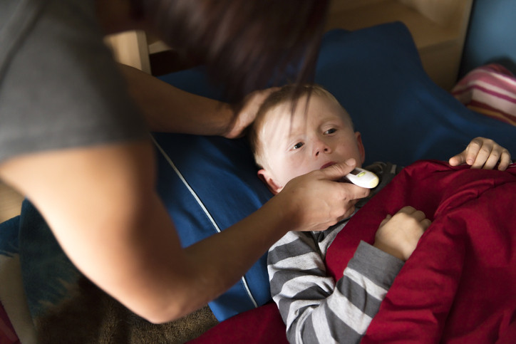 A sick boy lying in bed, his mother takes his temperature with an oral thermometer