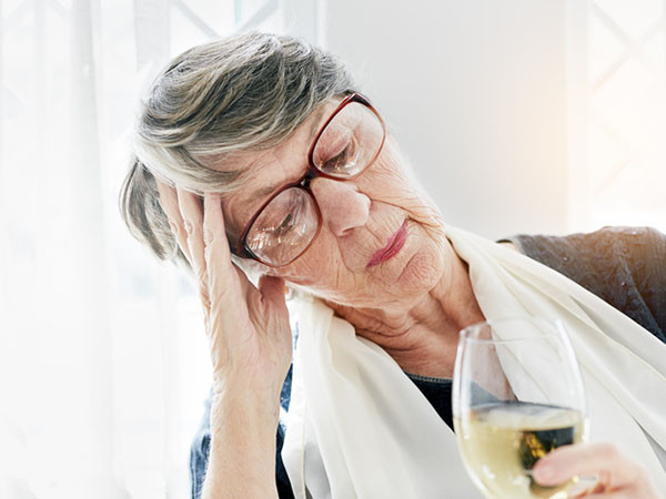 A mature woman holding a glass of wine, leaning on her elbow with her hand on her head