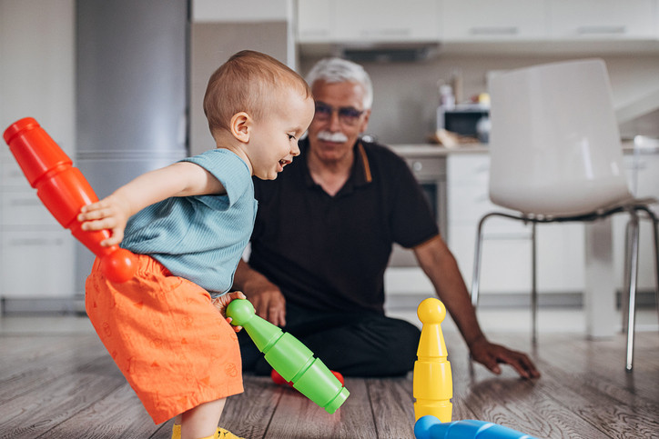 A grandfather watches his grandchild playing with toys