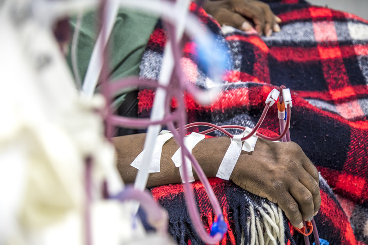 A partial view of a person having dialysis that shows twisting intravenous tubes going into one forearm arm; his other hand is on top of a plaid blanket