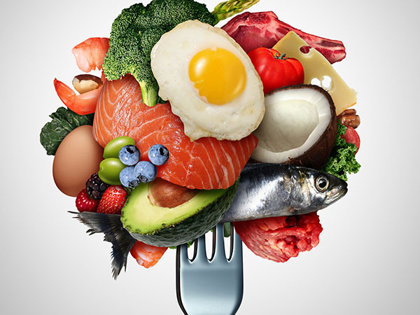 A fork with a collection of foods on top of it: brocolli, shrimp, raw fish, raw meet, cheese, berries, a coconut, and and egg