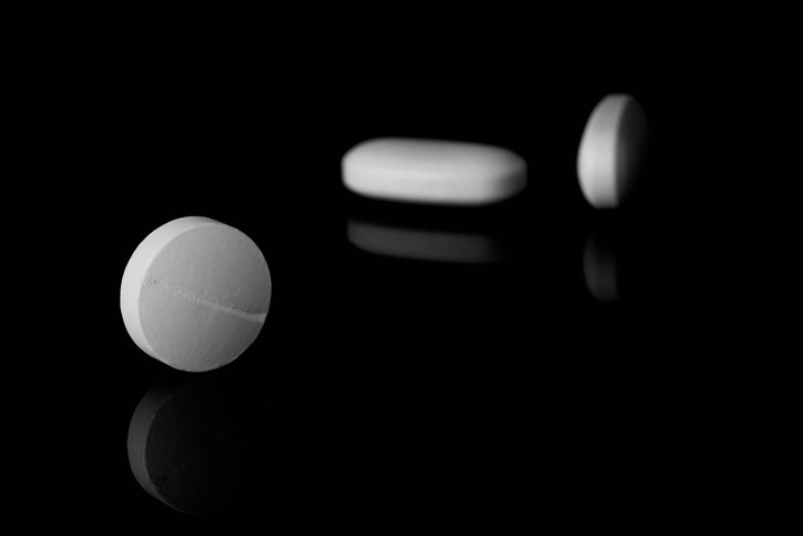 A white pill in foreground and two white tablets against a dark background