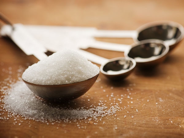 Metal measuring spoons on a wooden surface, the largest one is overflowing with sugar
