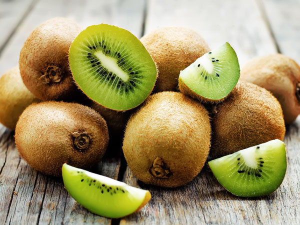 close-up of a pile of kiwi fruit whole and cut arranged on rough unfinished wood planks