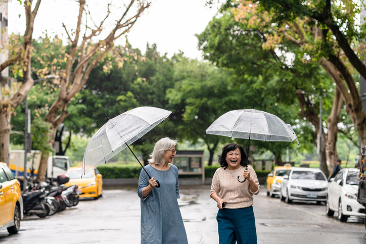 Two smiling women on a walk together outdoors, they're holding umbrellas