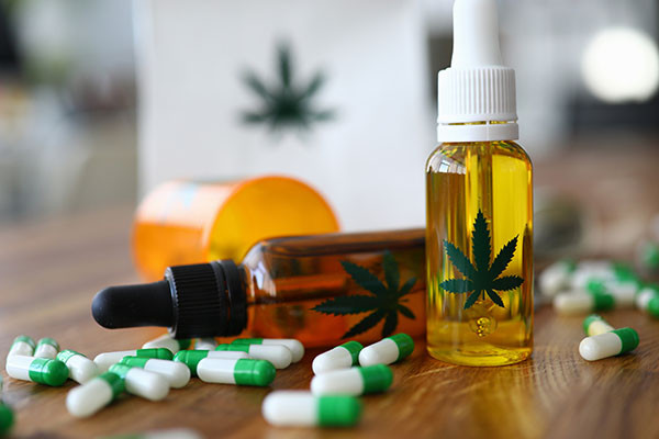 close-up photo of medical marijuana products: green and white capsules spread on a table and a bottle of CBD oil with a small logo of a marijuana leaf on it