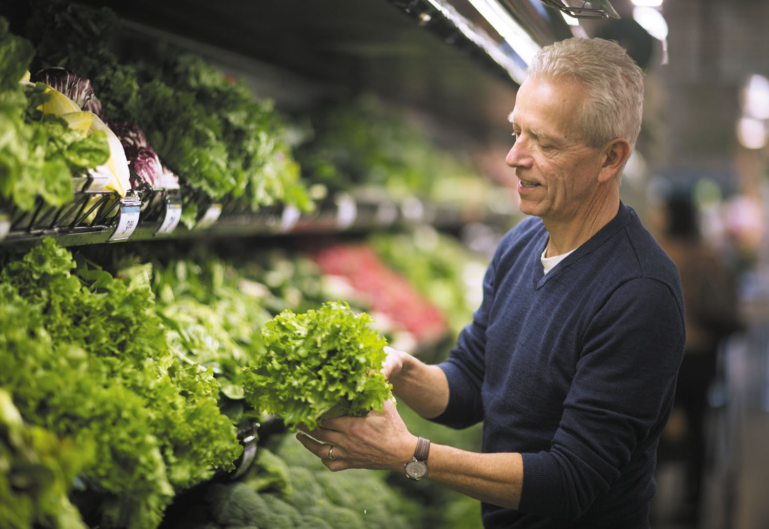 photo of a man choosing leafy greens from a supermarket produce section