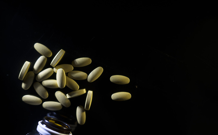 Multivitamins spilling upward out of a bottle against a dark background