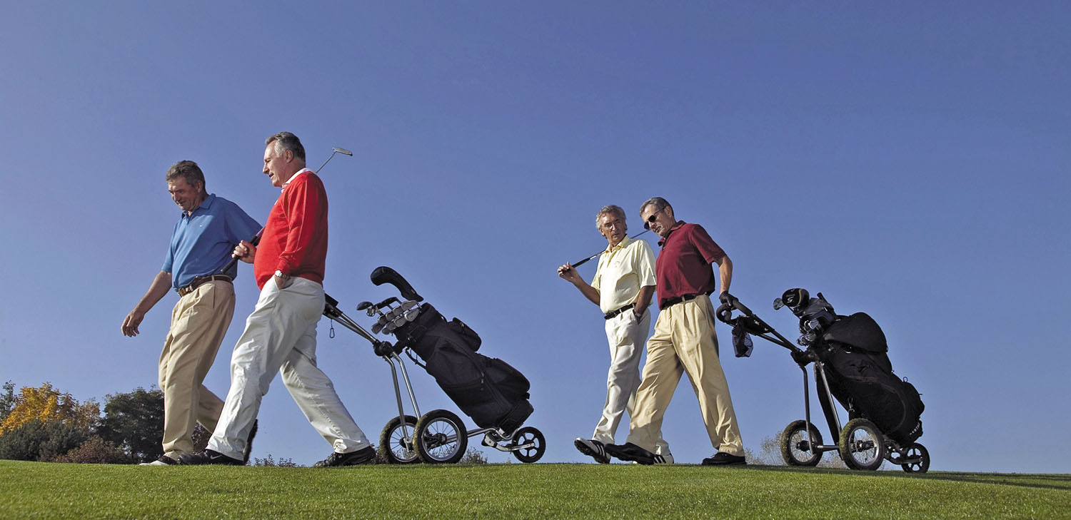 photo of four men walking on a golf course, pulling wheeled carts that hold their clubs