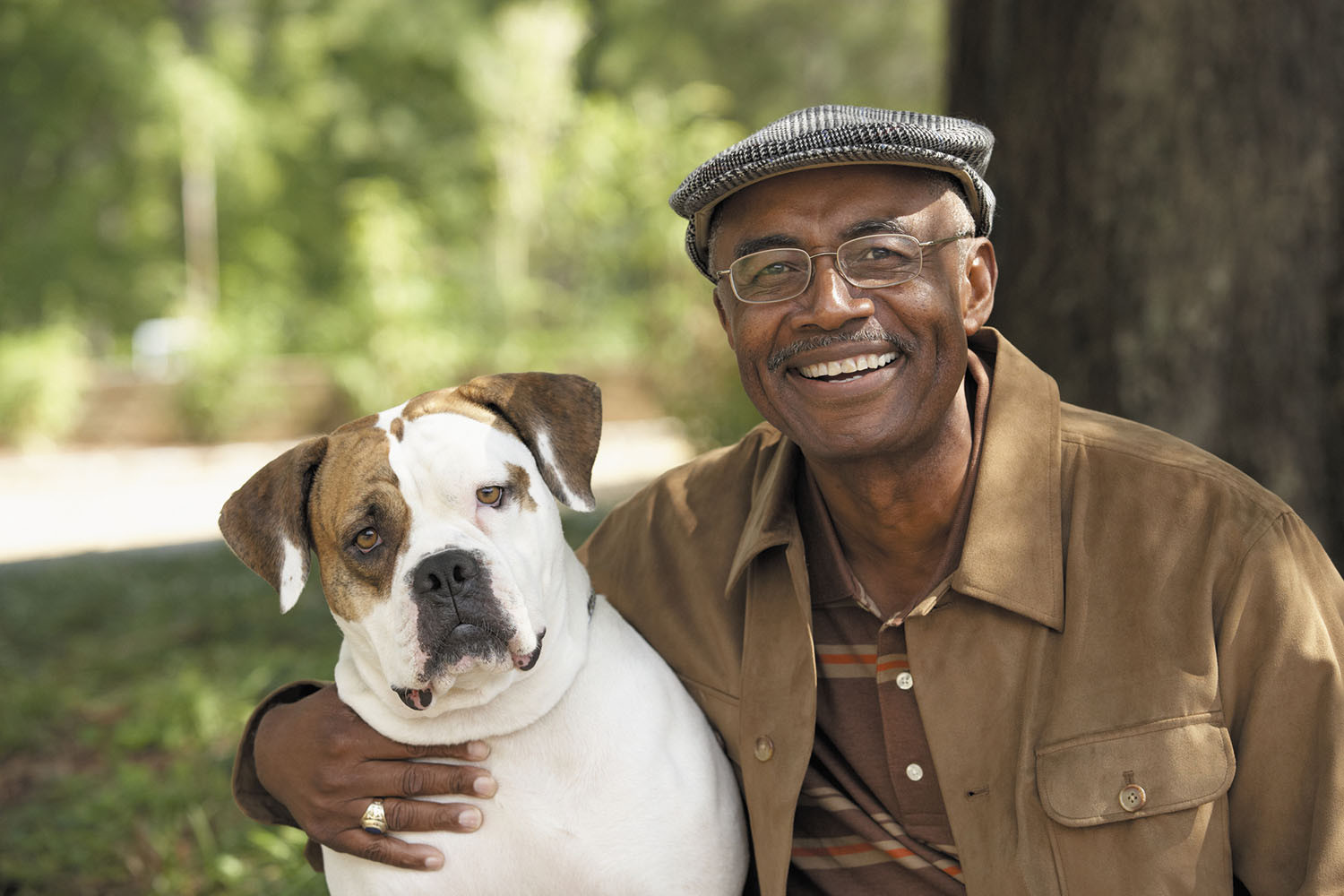 photo of a smiling man posing with his dog outdoors in front of a tree
