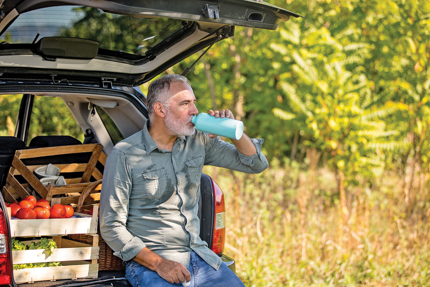 photo of an older man drinking water while sitting at the open back of a car