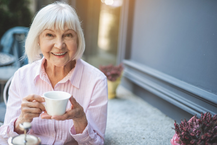Photo of older woman smiling and holding cup of tea, outside