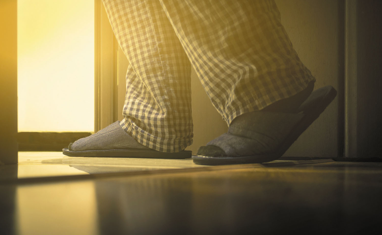 photo of the legs and feet of a man wearing pajamas and slippers walking into a bathroom at night