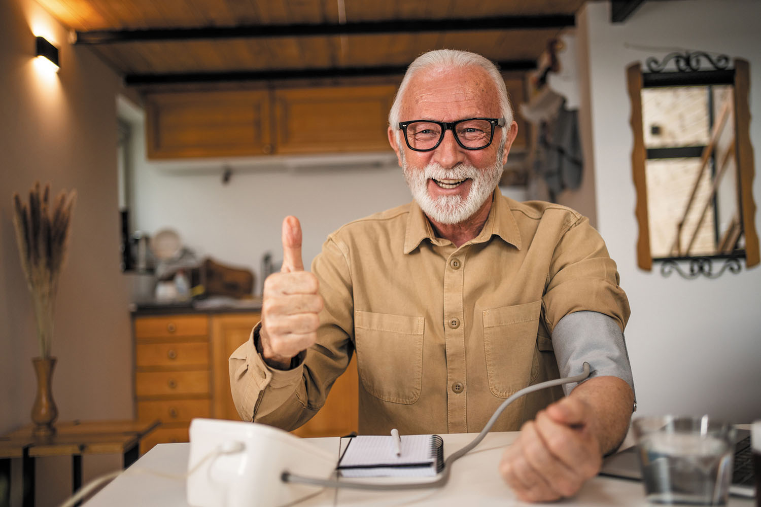 photo of a senior man smiling and making a thumbs-up gesture while taking his blood pressure at home
