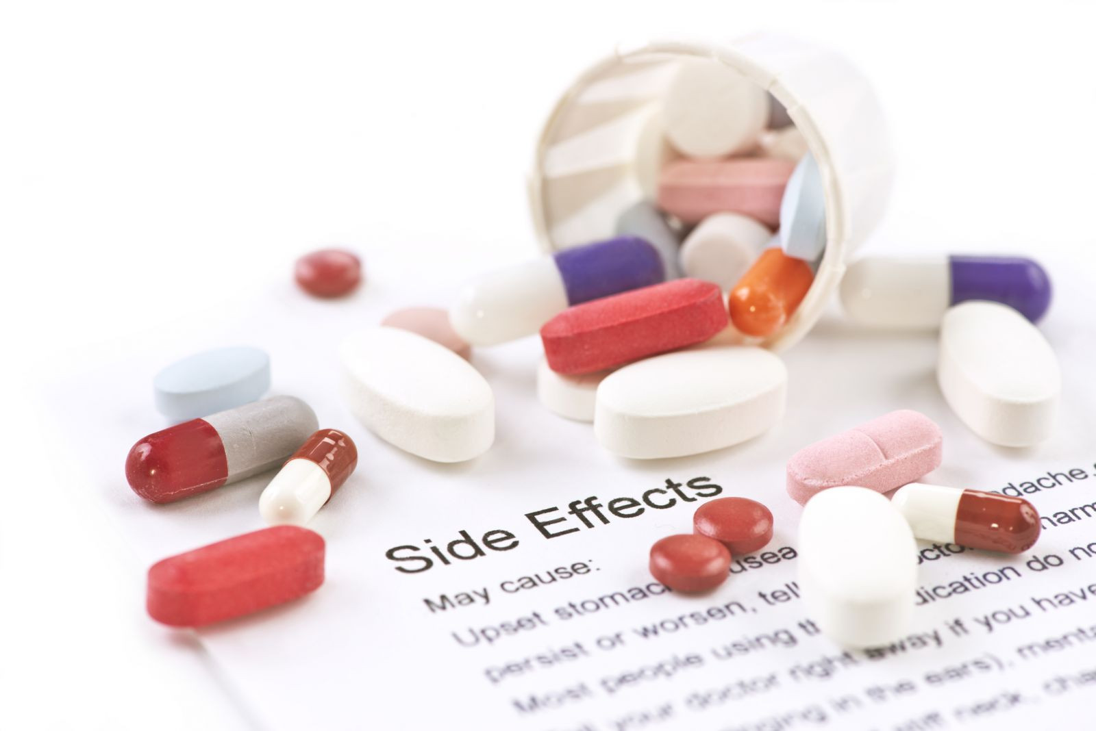 photo of an assortment of pills spilling out of a paper cup onto a piece of paper titled side effects