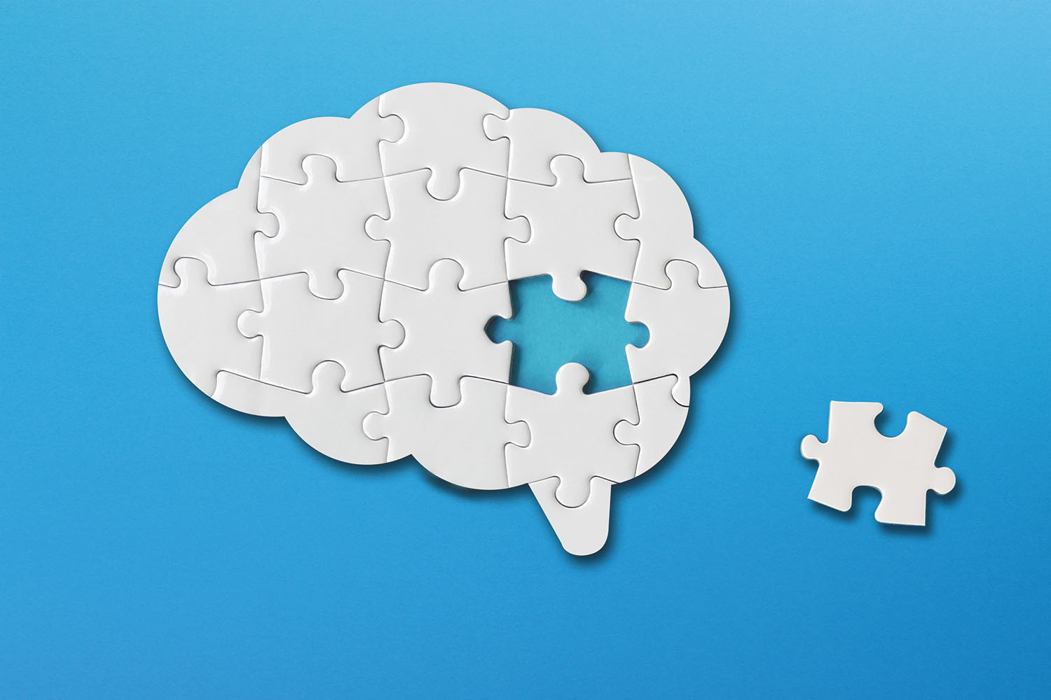 illustration of a puzzle in the shape of a brain with one piece removed and set to the side, all against a blue background