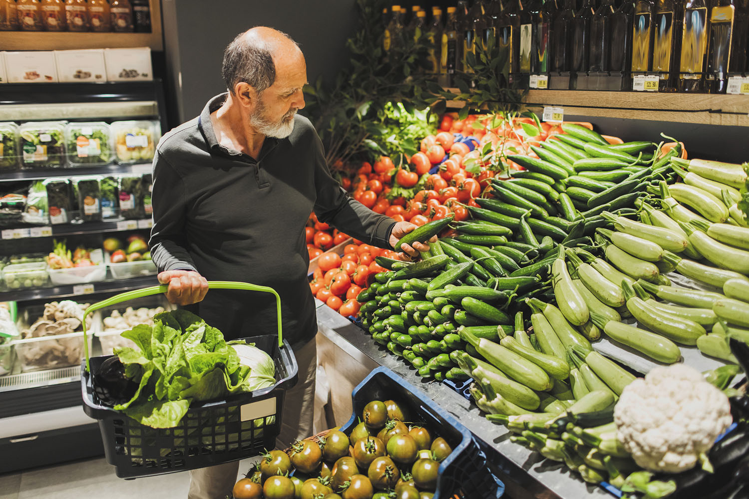 photo of a man shopping in the product department of a supermarket while holding a basket full of fresh food selections