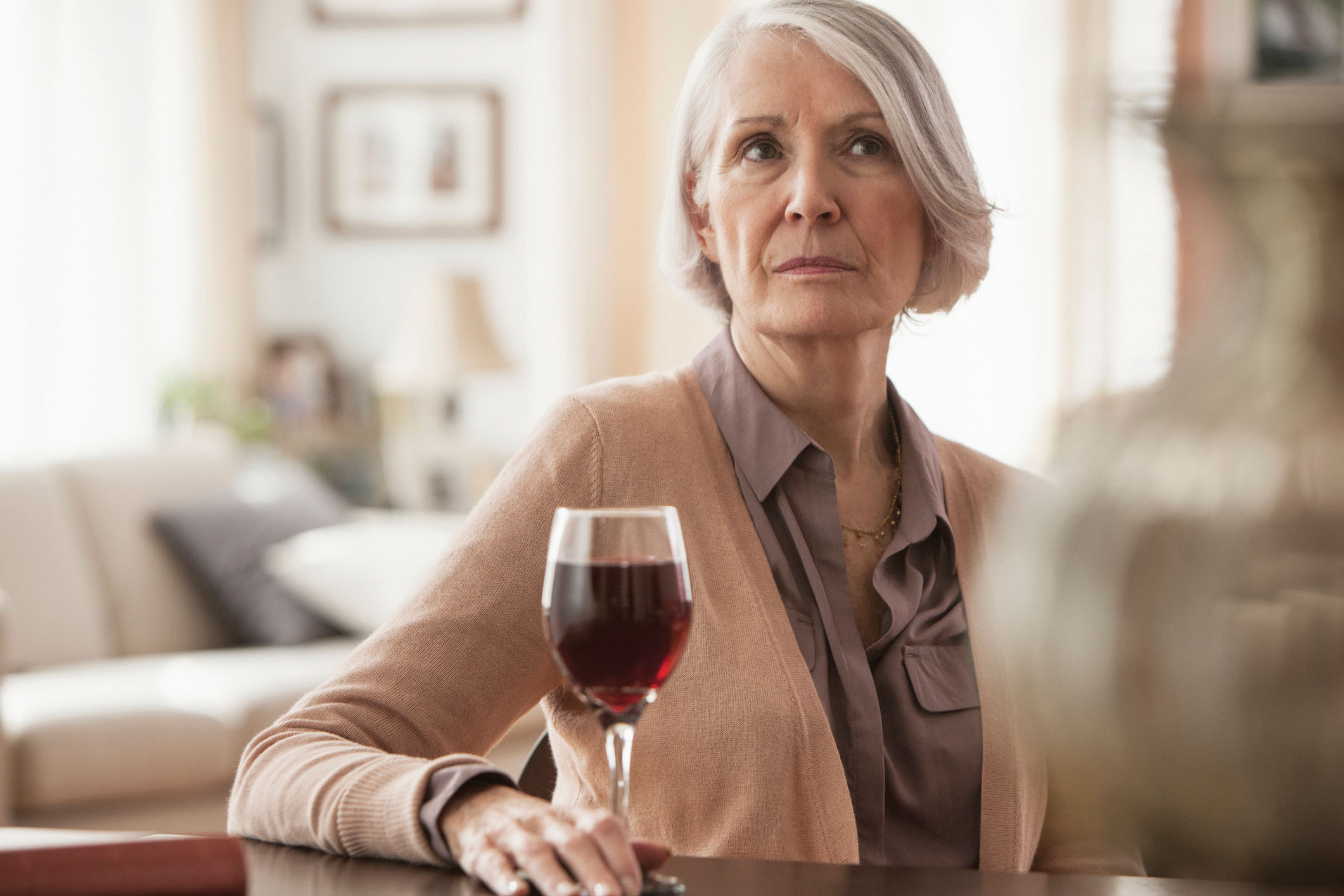 photo of a mature woman at home with a glass of red wine, looking serious and concerned