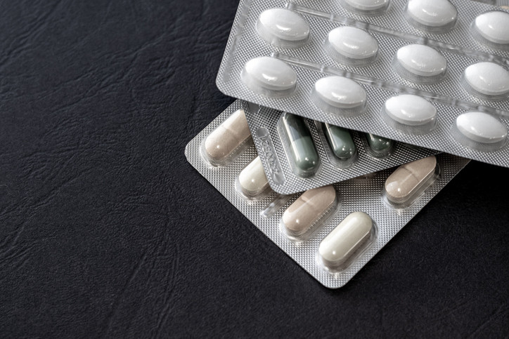 photo of blister packs of medications stacked in a pile, pills are white, green and yellow