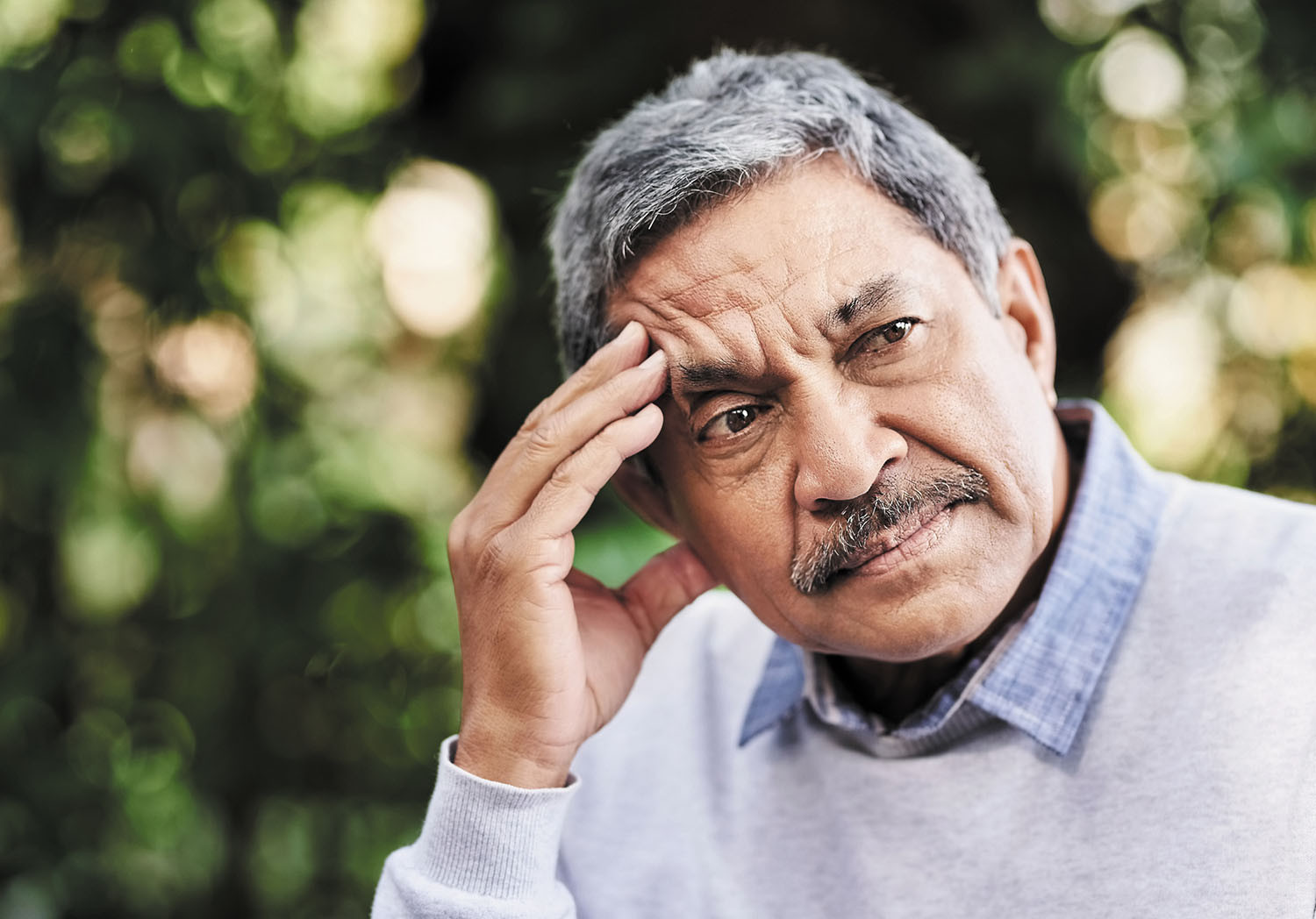 photo of a senior man sitting outdoors holding his hand to his head as he tries to remember something