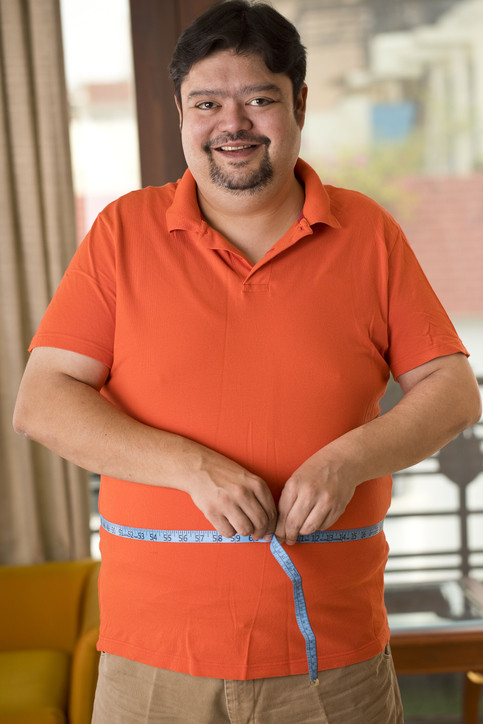 A photo of an overweight man measuring his waist size with tape measure.