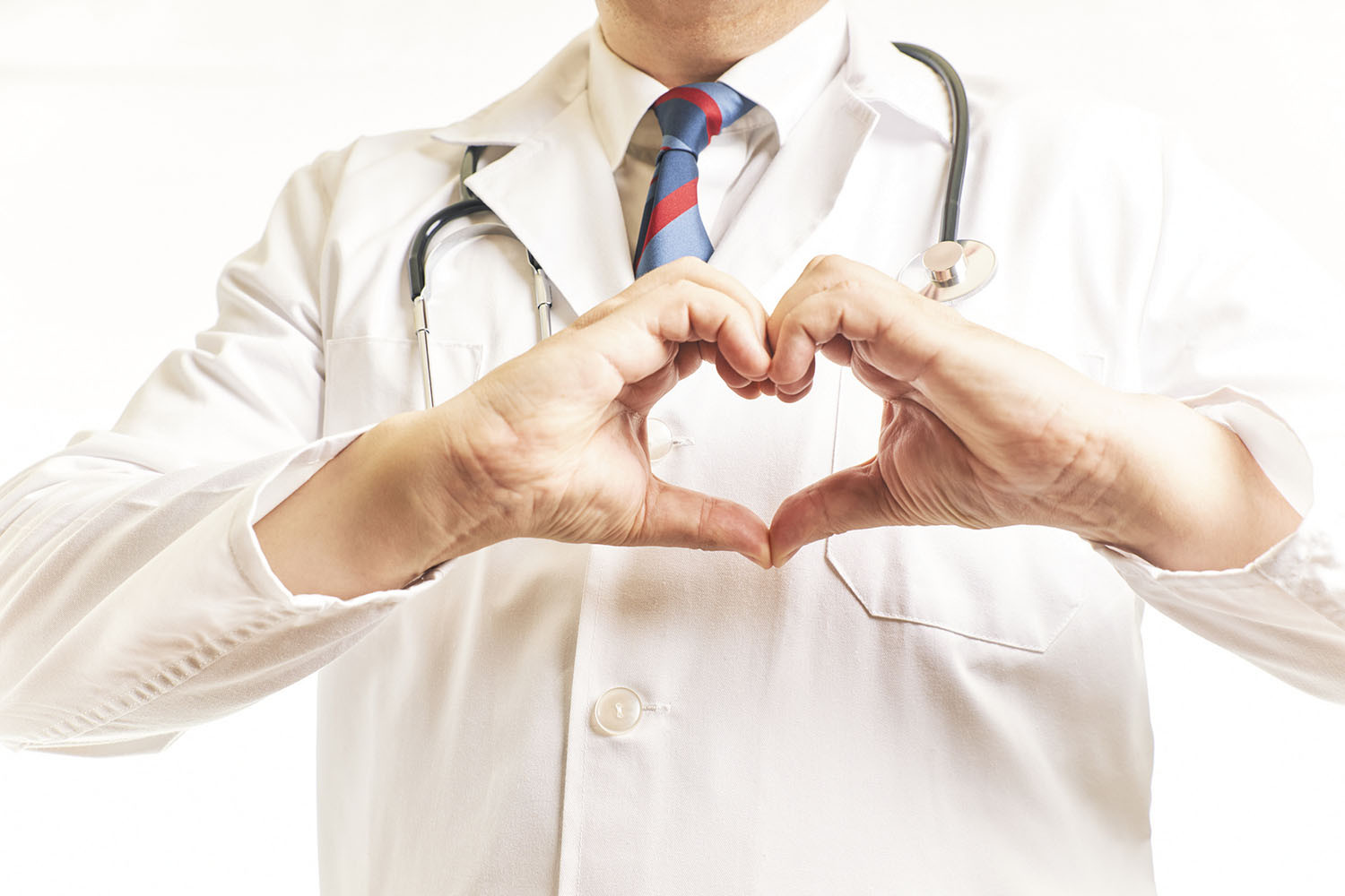 cropped photo showing the torso and arms of a doctor wearing a white lab coat with a stethoscope around his neck holding his hands in front of him making the shape of a heart