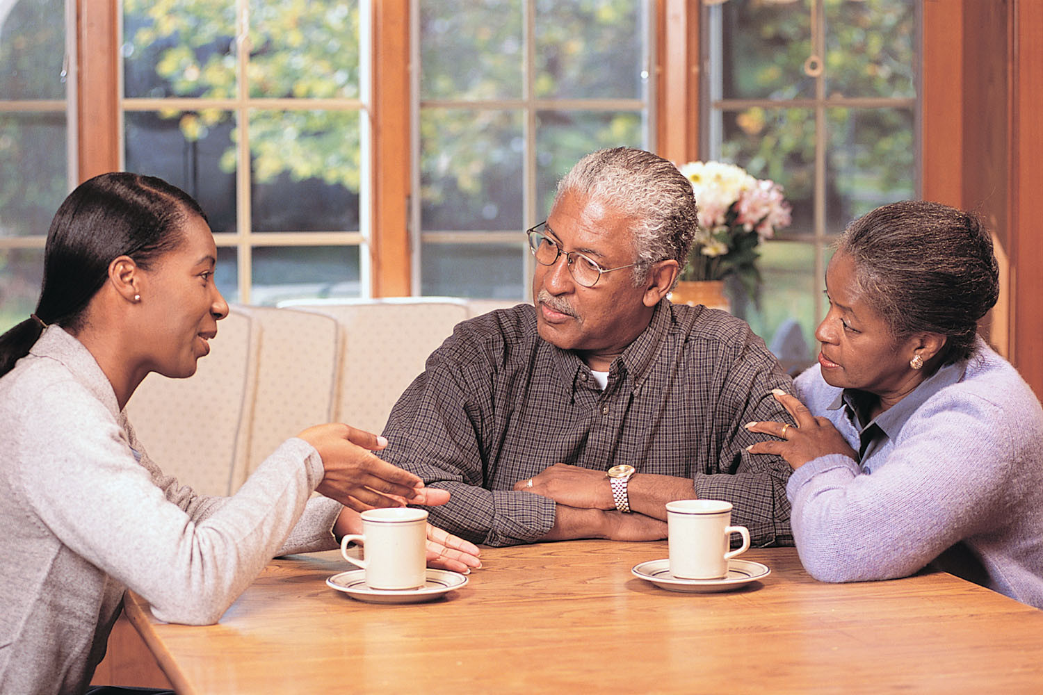 photo of a young woman speaking with her parents as they sit at a table in their home