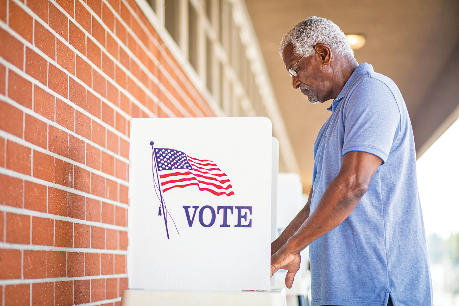photo of a mature man standing at a voting booth on a covered outdoor walkway