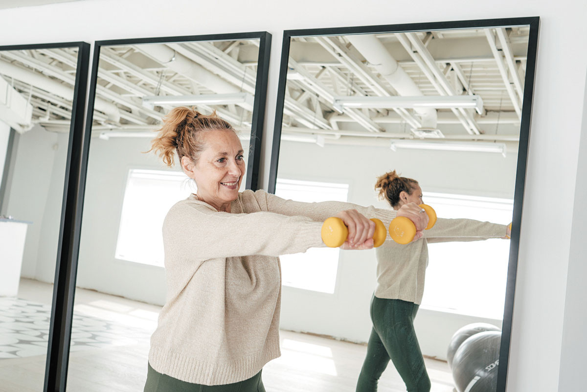 photo of a woman exercising with hand weights next to a mirror