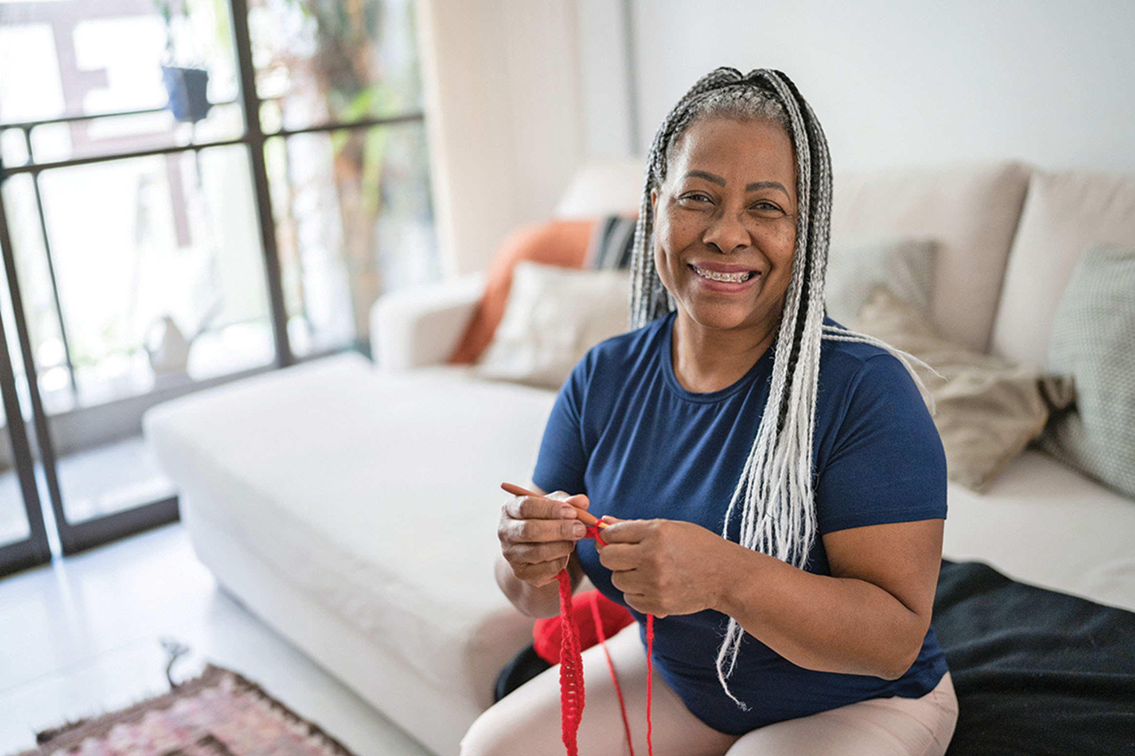 photo of an older woman with traditional braces smiling while sitting in her home and holding knitting needles and yarn