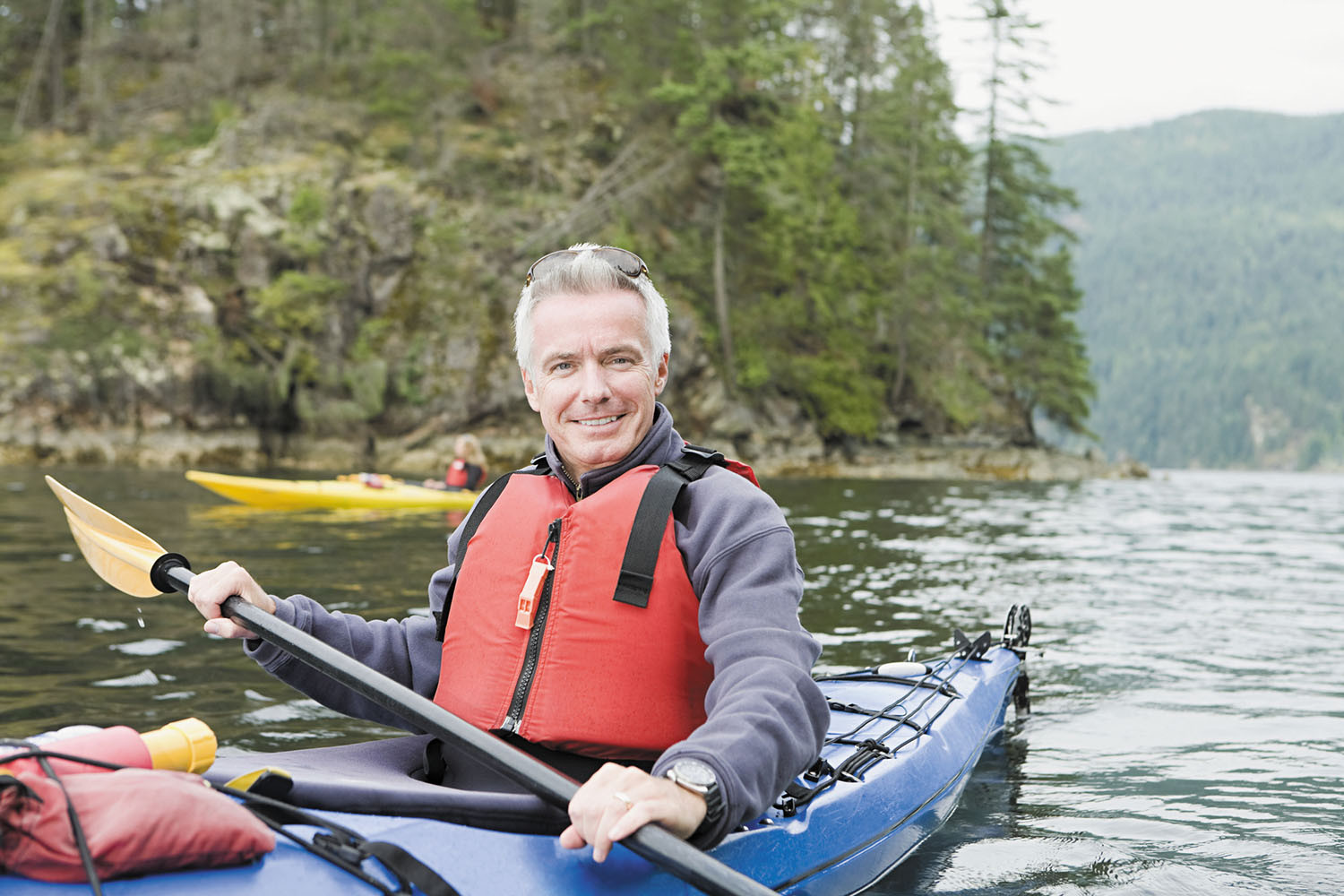 photo of a man paddling a kayak and wearing a safety flotation vest